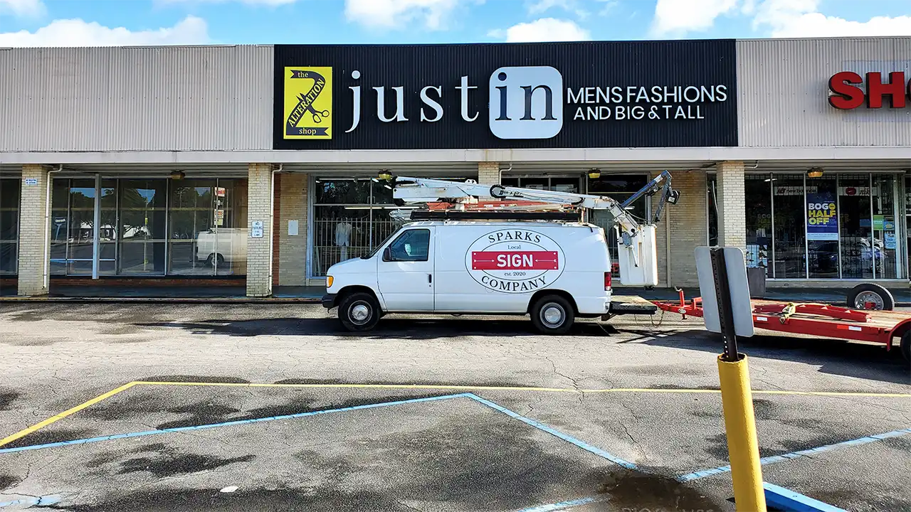 The Sparks Sign Company van with its lift parked under the Just In Mens Fashions storefront sign