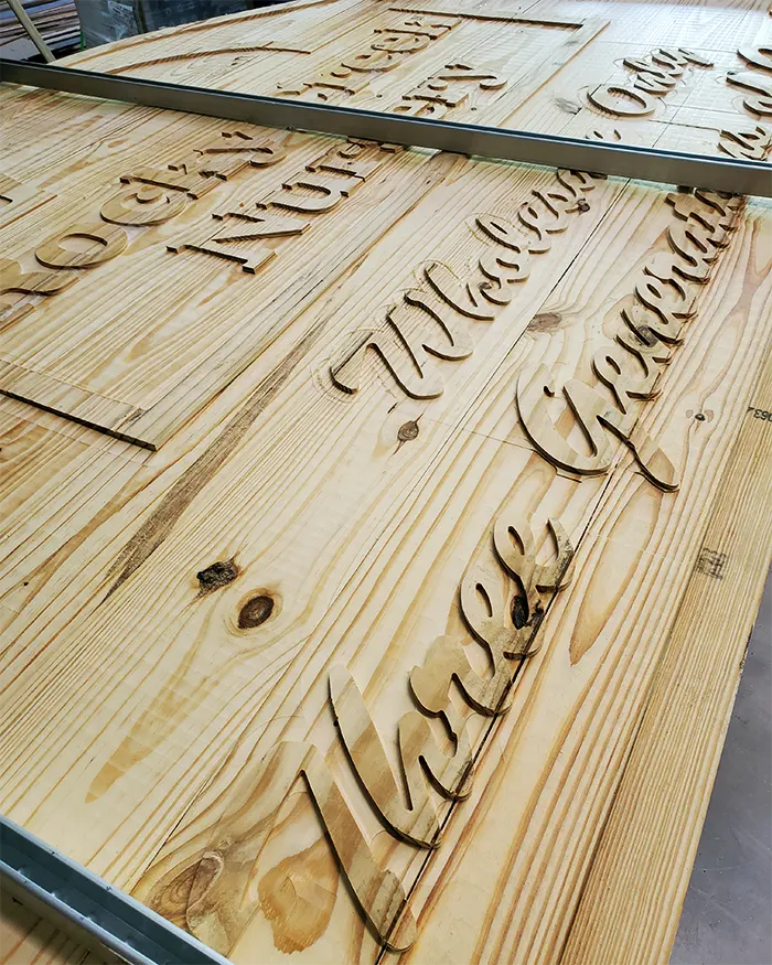 Routed wooden signs being made in the shop: script lettering cut into pine boards on a CNC table