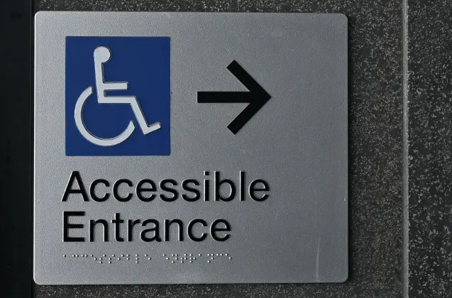 An Accessible Entrance plaque with the wheelchair symbol, an arrow and Braille