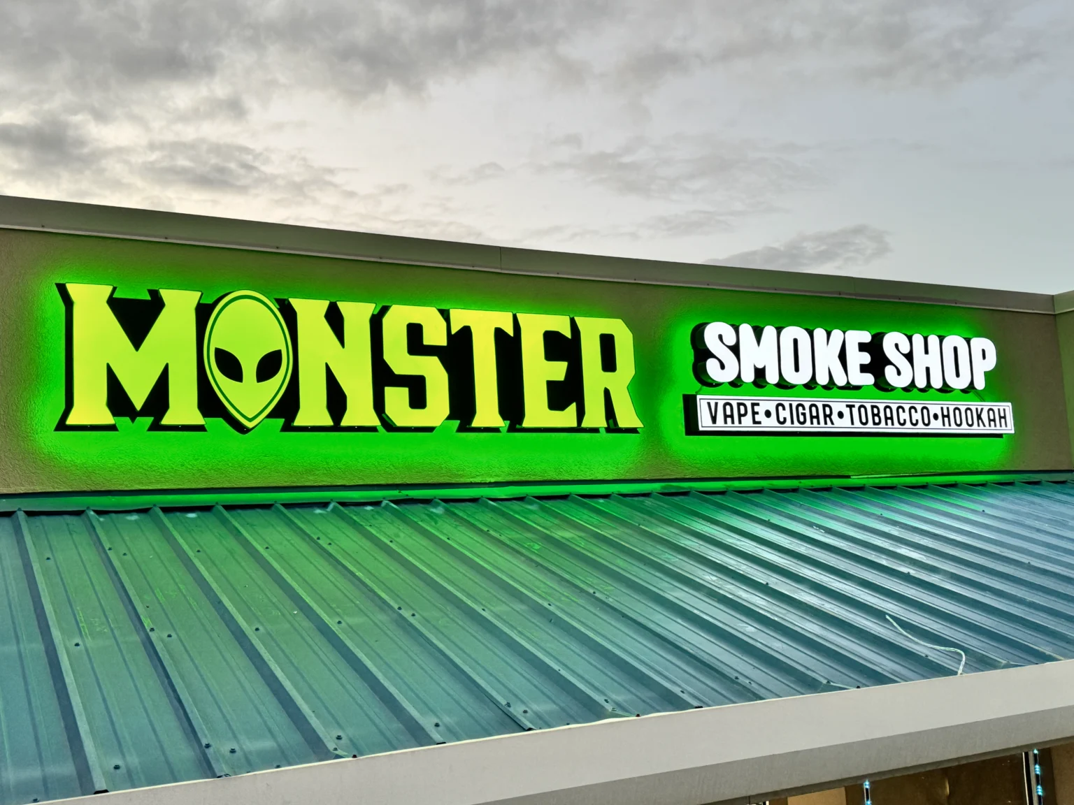 Green illuminated channel letters on the Monster Smoke Shop storefront