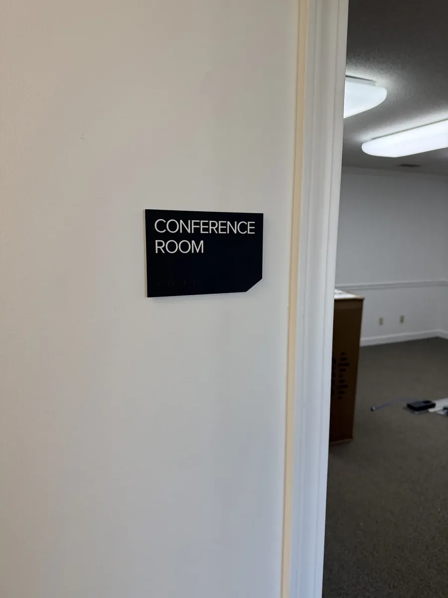 A black Conference Room sign with raised letters and Braille on the wall next to an open doorway into the room
