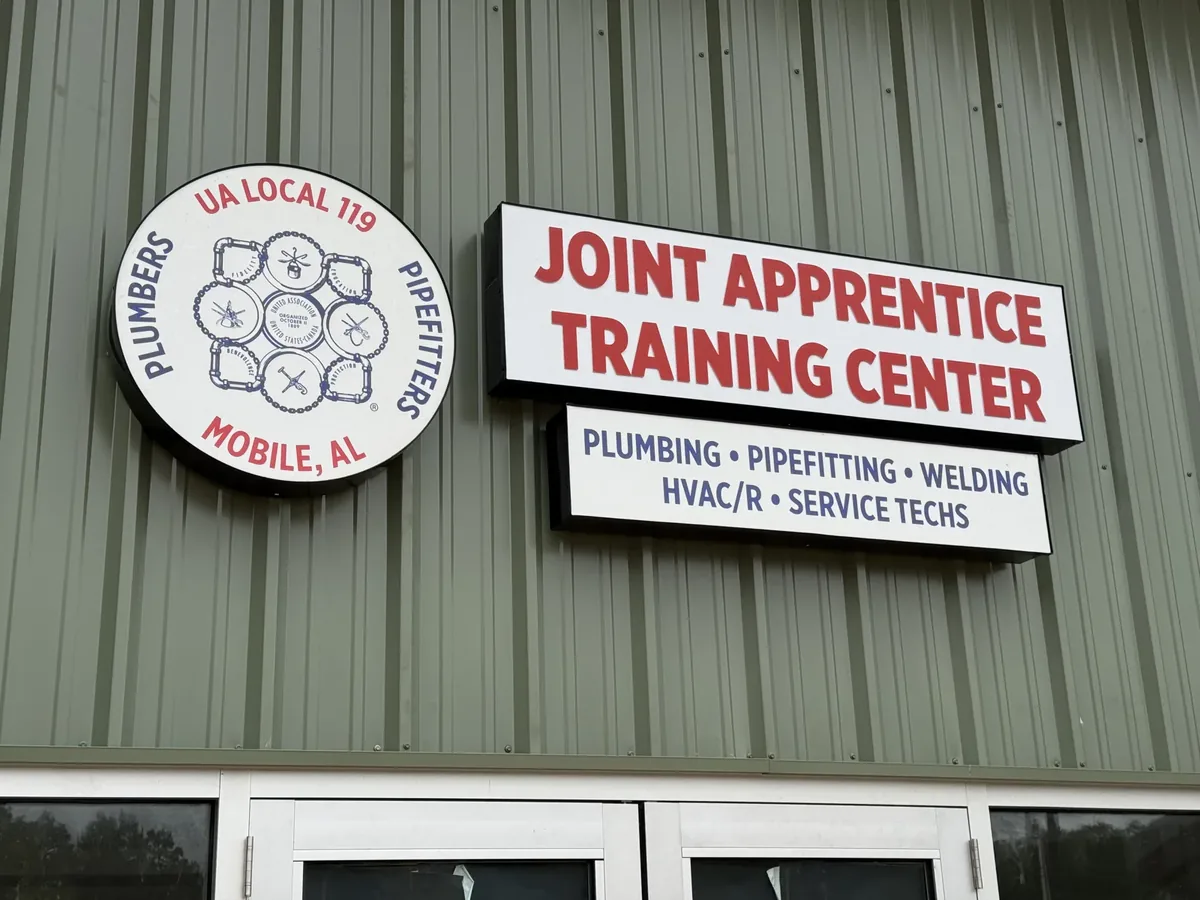 The Joint Apprentice Training Center cabinet signs, red letters over a blue-lettered panel beside a round union logo, on a green metal building