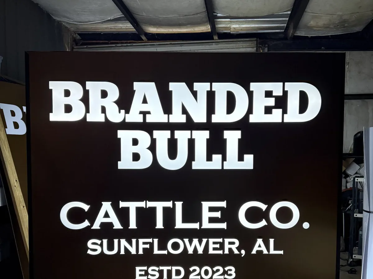A lit light box with white letters glowing on a dark brown face, standing indoors before installation