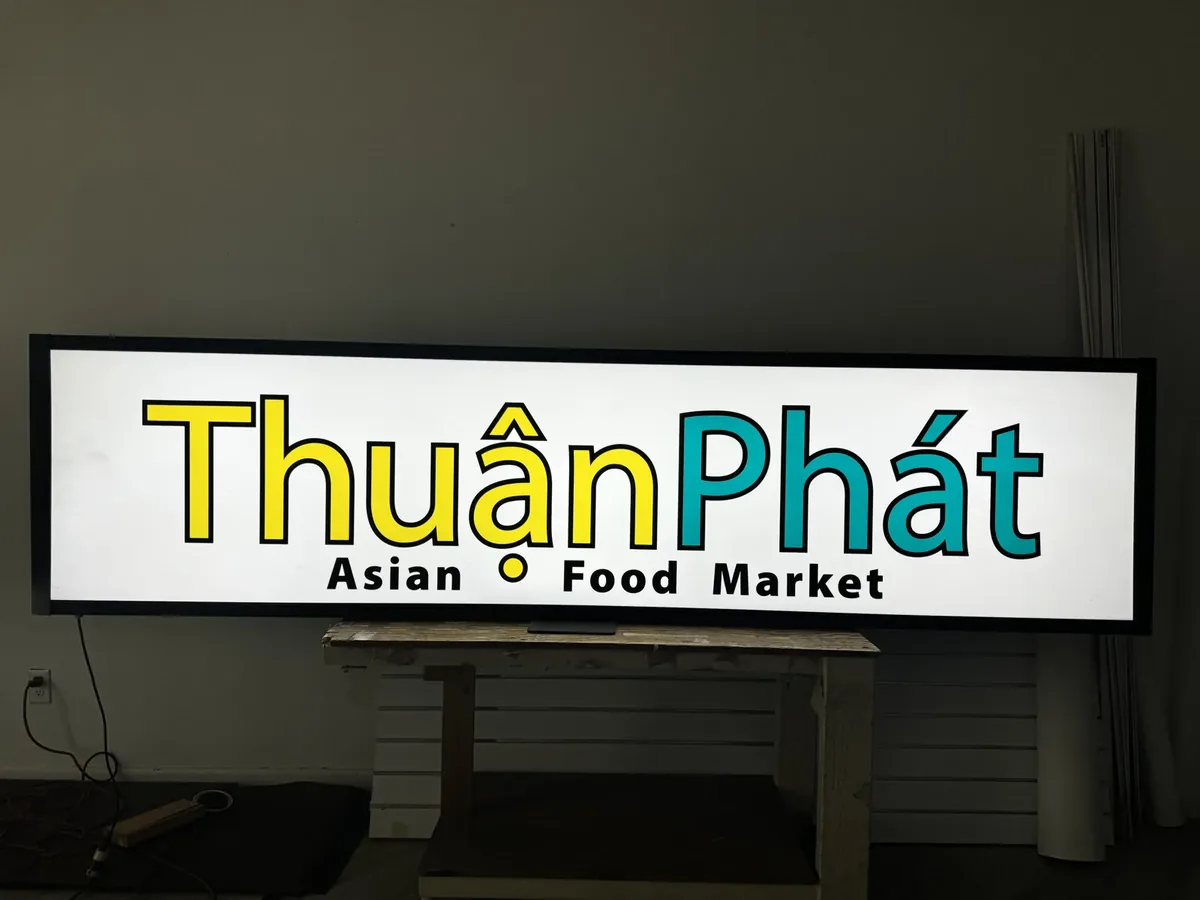 A lit light box with yellow and teal lettering standing indoors before installation