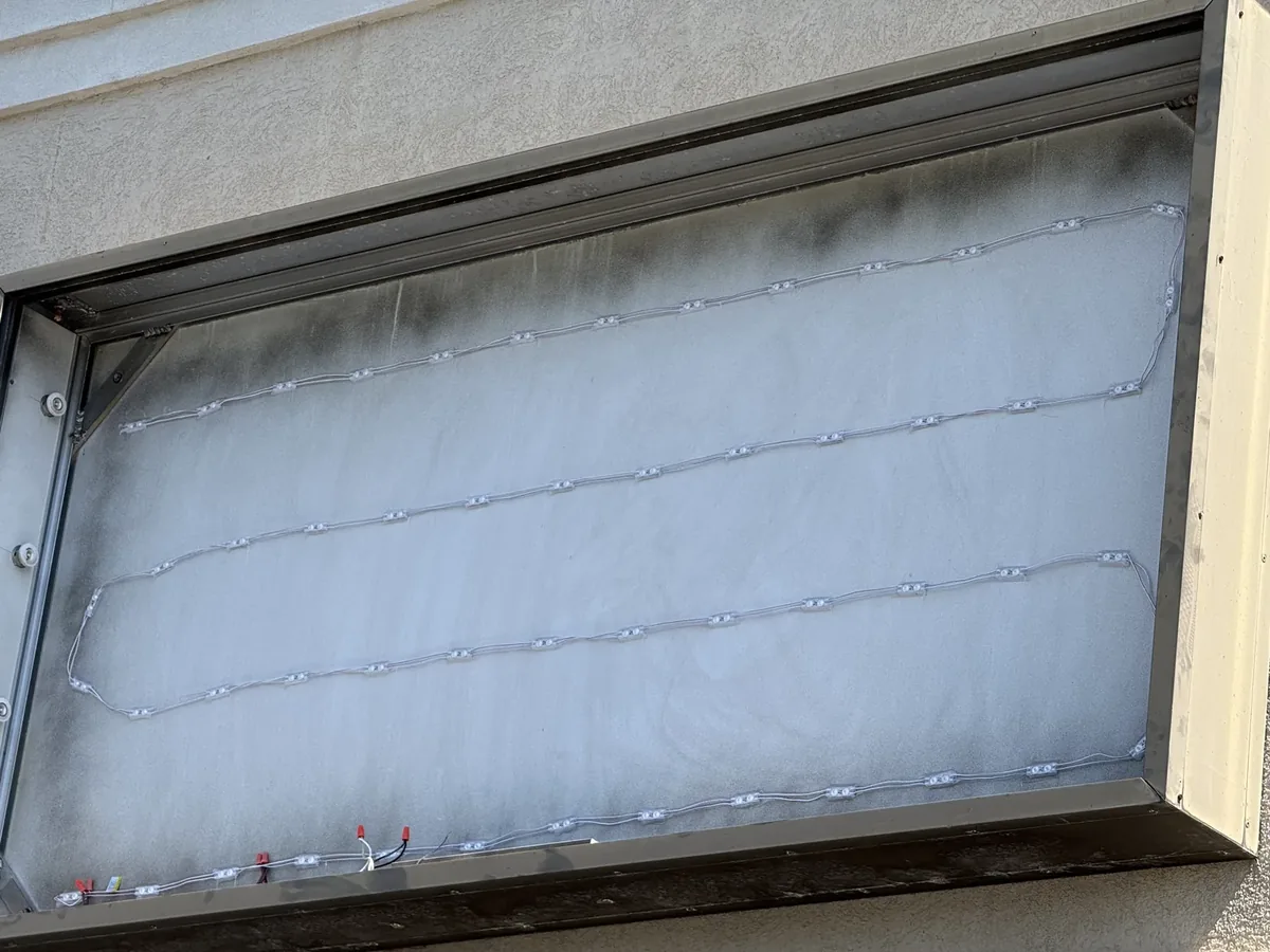 A sign cabinet open on a storefront wall before its face went in, strings of LED modules wired across its white back