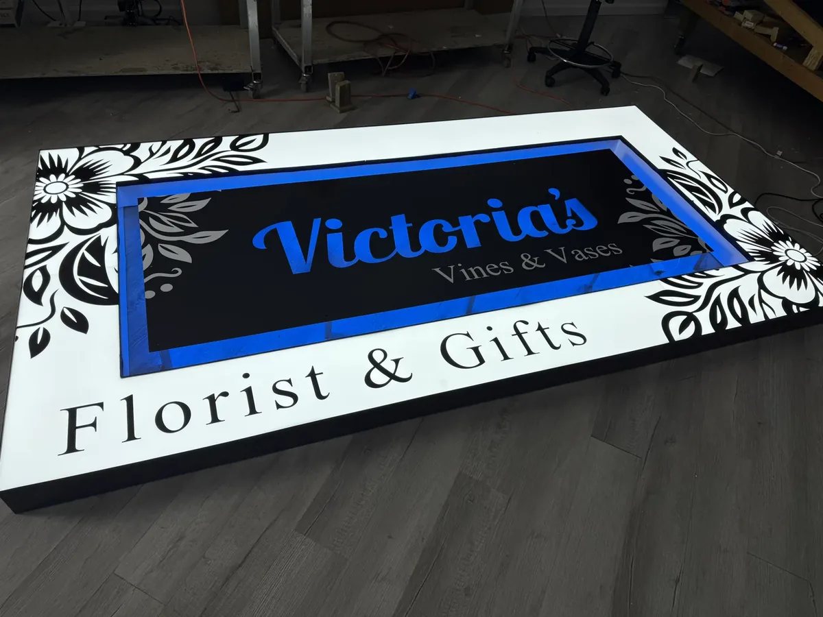 Victoria's Vines & Vases cabinet sign lit blue, lying face up on a shop floor