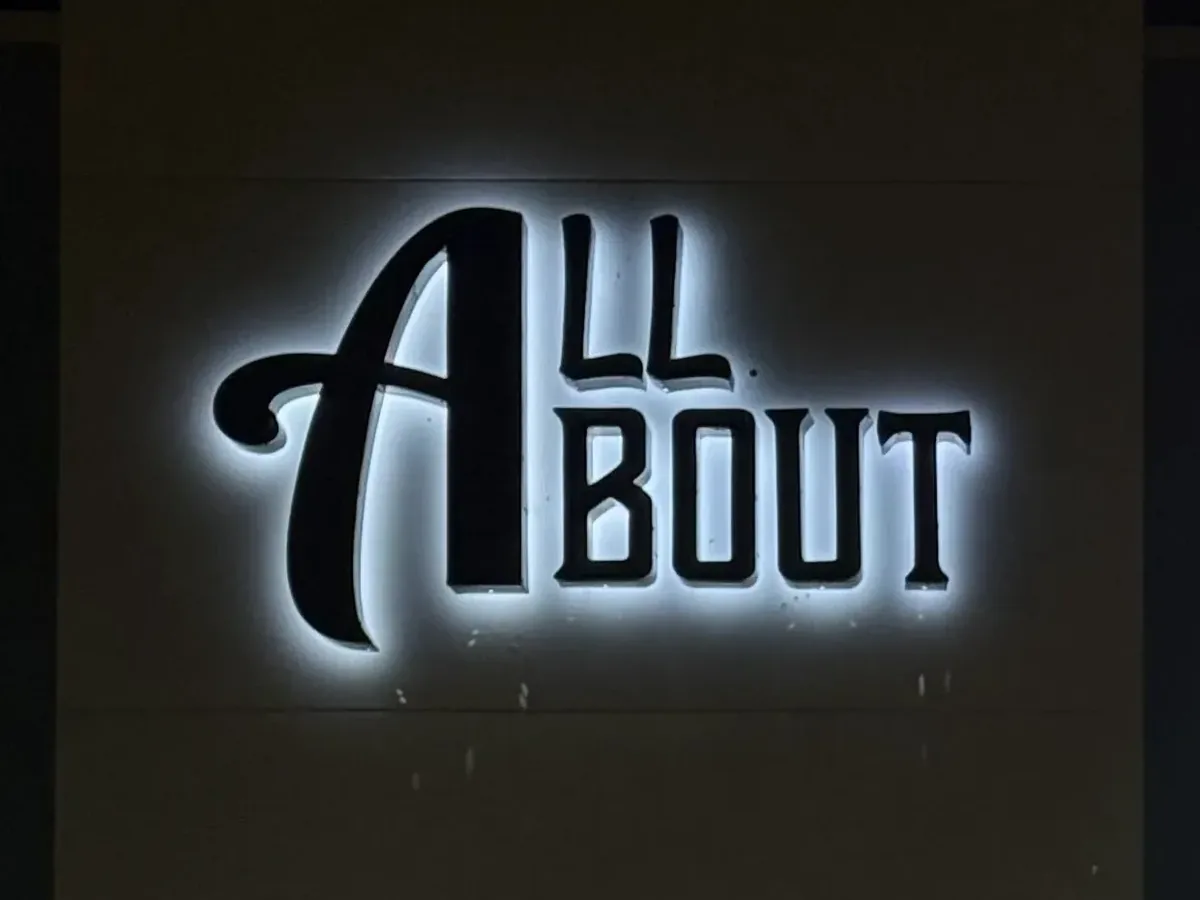 Halo-lit channel letters on a storefront at night, solid dark faces with white light glowing on the wall behind them