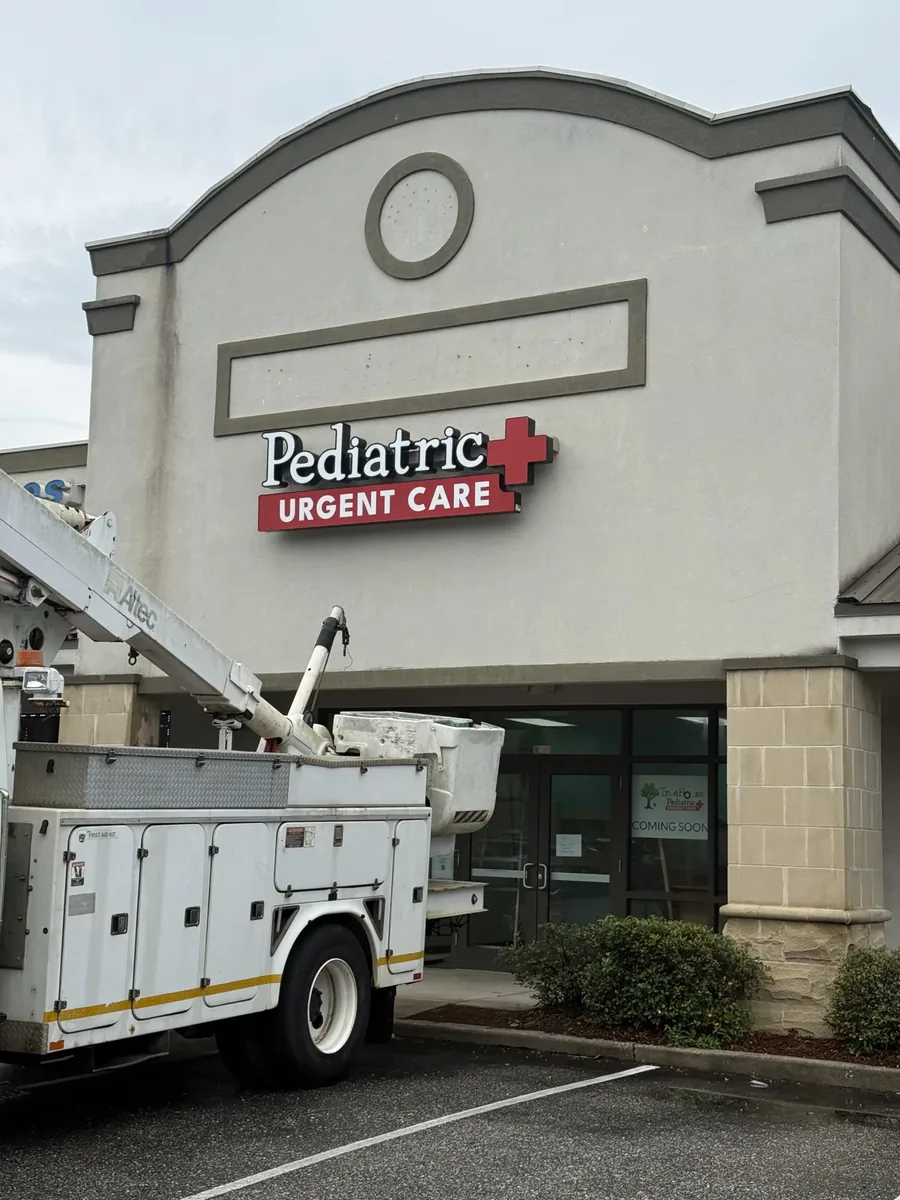 A bucket truck with its boom raised, parked below newly installed channel letters on a shopping center tower during a sign install
