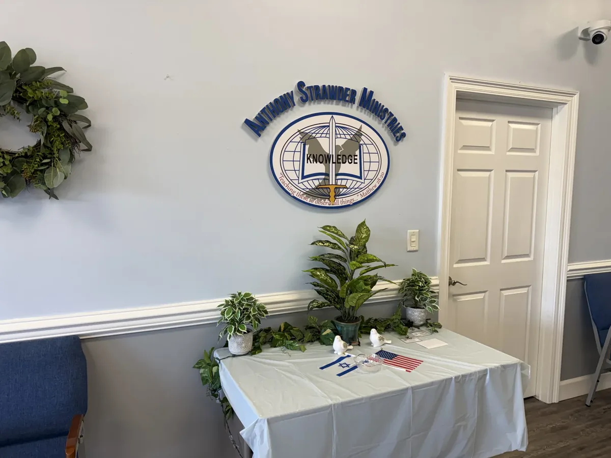 Anthony Strawder Ministries dimensional logo on a lobby wall beside a door, above a table with plants