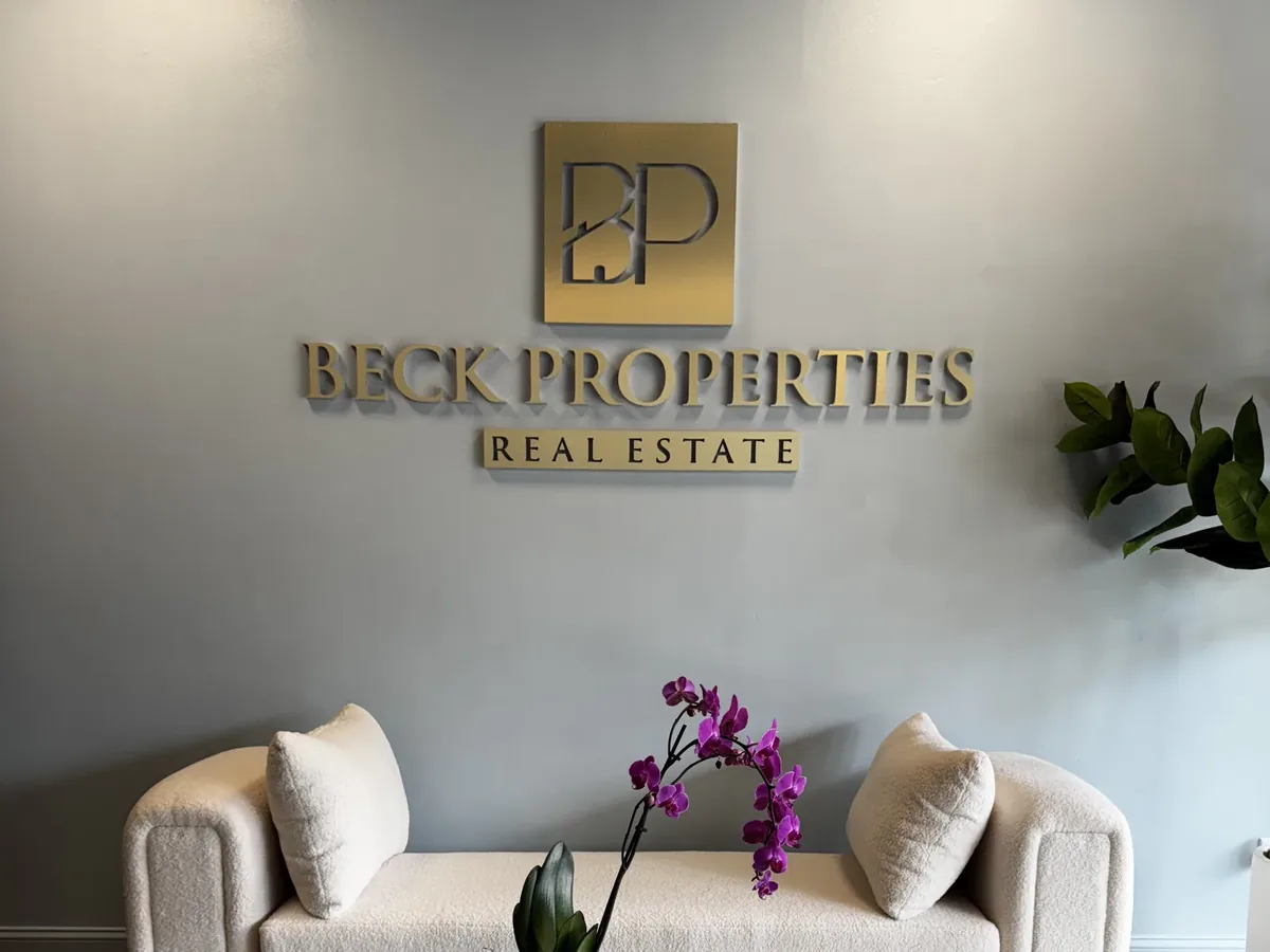 Beck Properties Real Estate gold dimensional logo on a lobby wall above a cream sofa