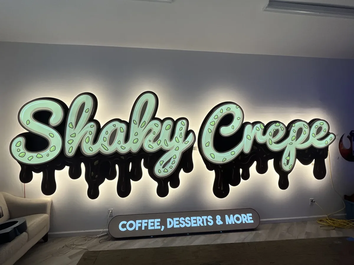 Lit dessert shop sign with mint letters and dark drips, glowing warm on an interior wall