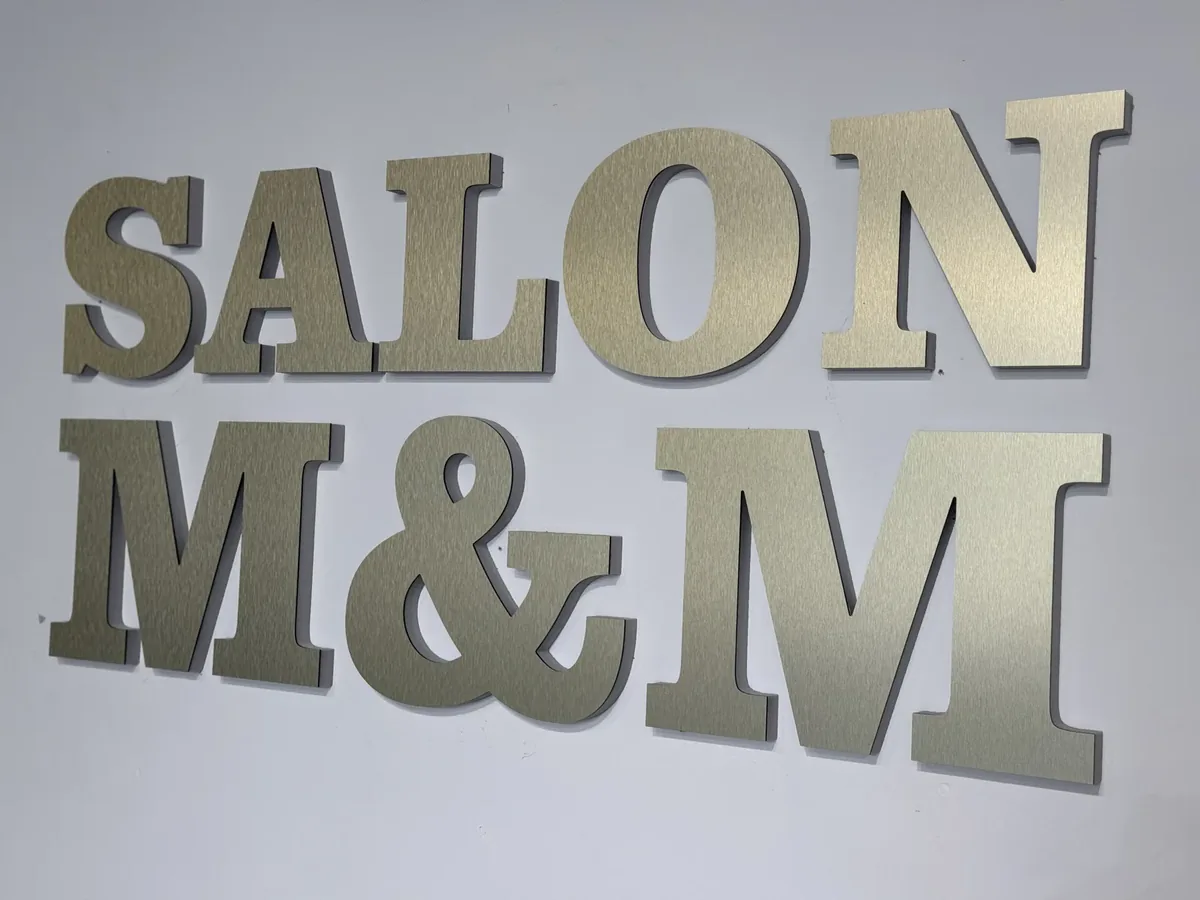 Salon M&M brushed metal dimensional letters on a light grey lobby wall
