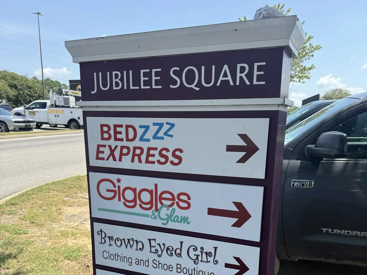 A shopping center directory sign with a named header cap and a stack of white tenant panels, each with a store name and a direction arrow
