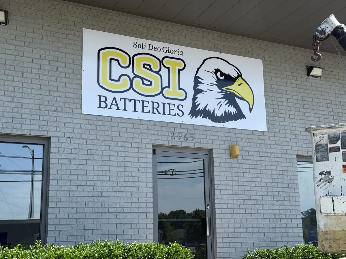 A flat panel sign with a yellow-lettered logo and an eagle mounted over a shop door on a painted brick wall