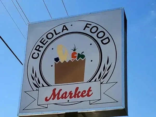 The Creola Food Market pylon sign cabinet high on its pole against a clear blue sky