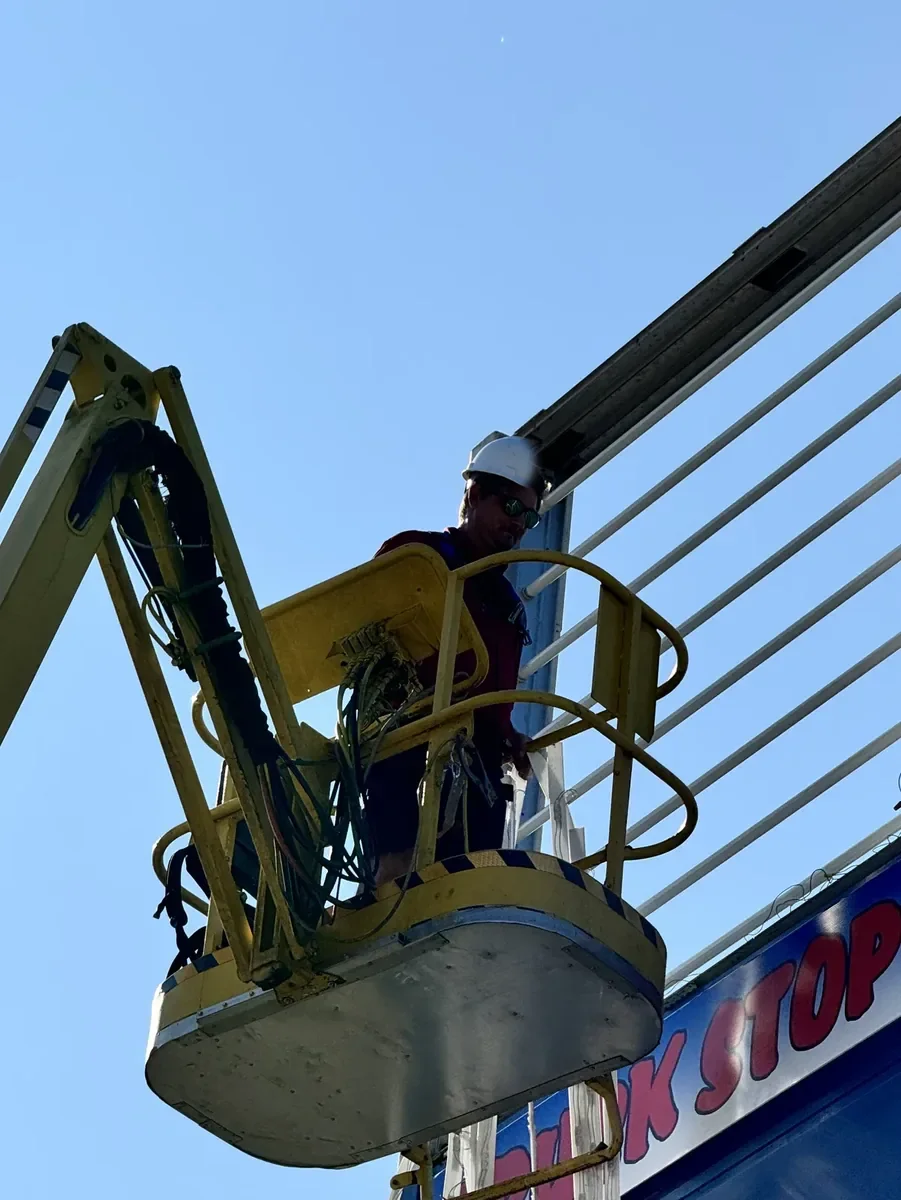 Crew member in a boom lift's basket at the top of a pylon sign's steel frame