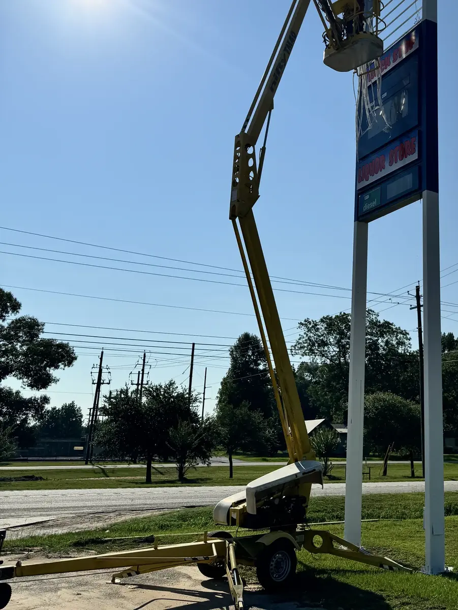 Crew member on a towable boom lift at the top of a tall two-post pylon sign