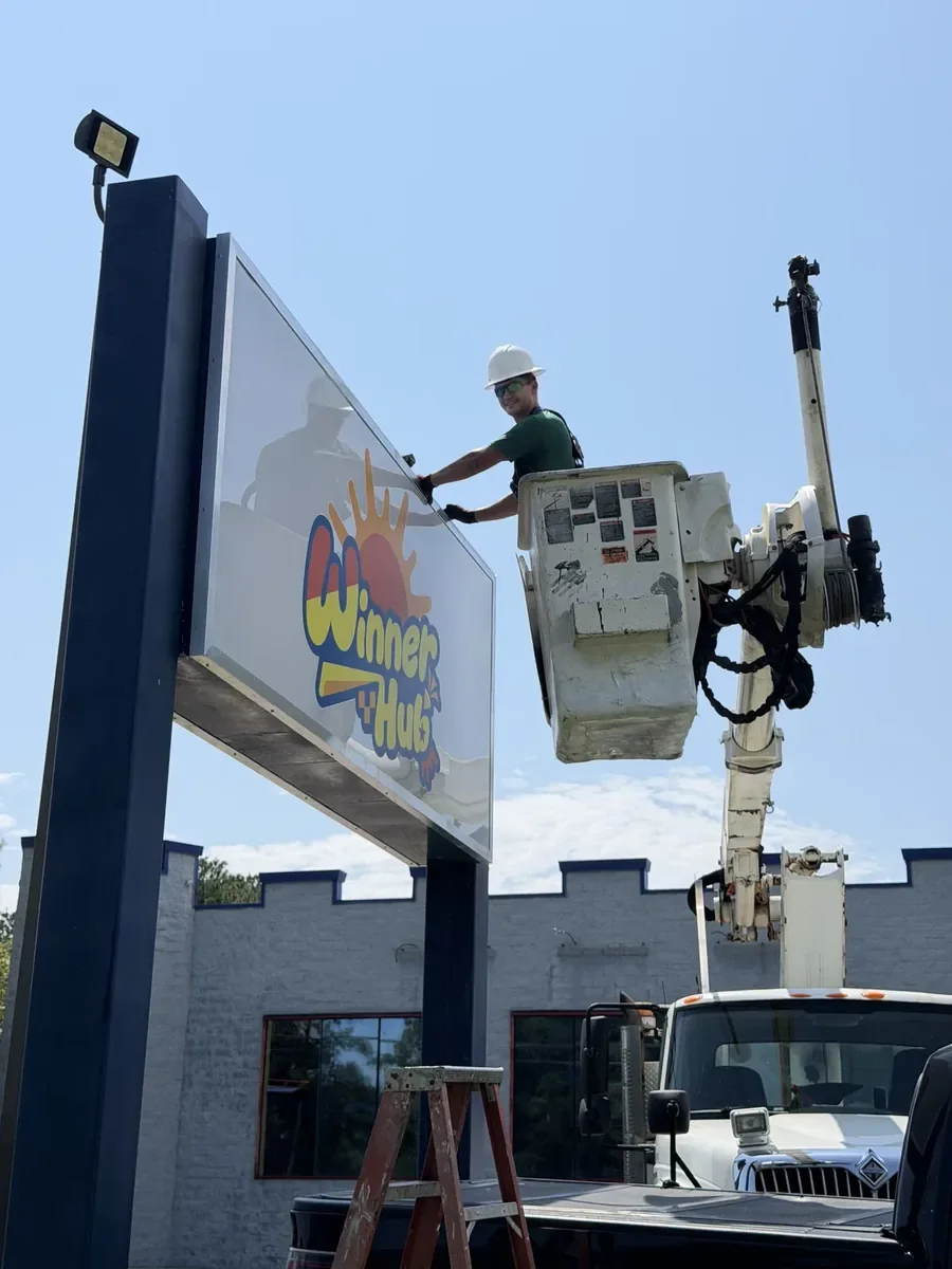 Installer in a bucket truck's bucket fitting the Winner Hub face onto its two-post pylon sign cabinet