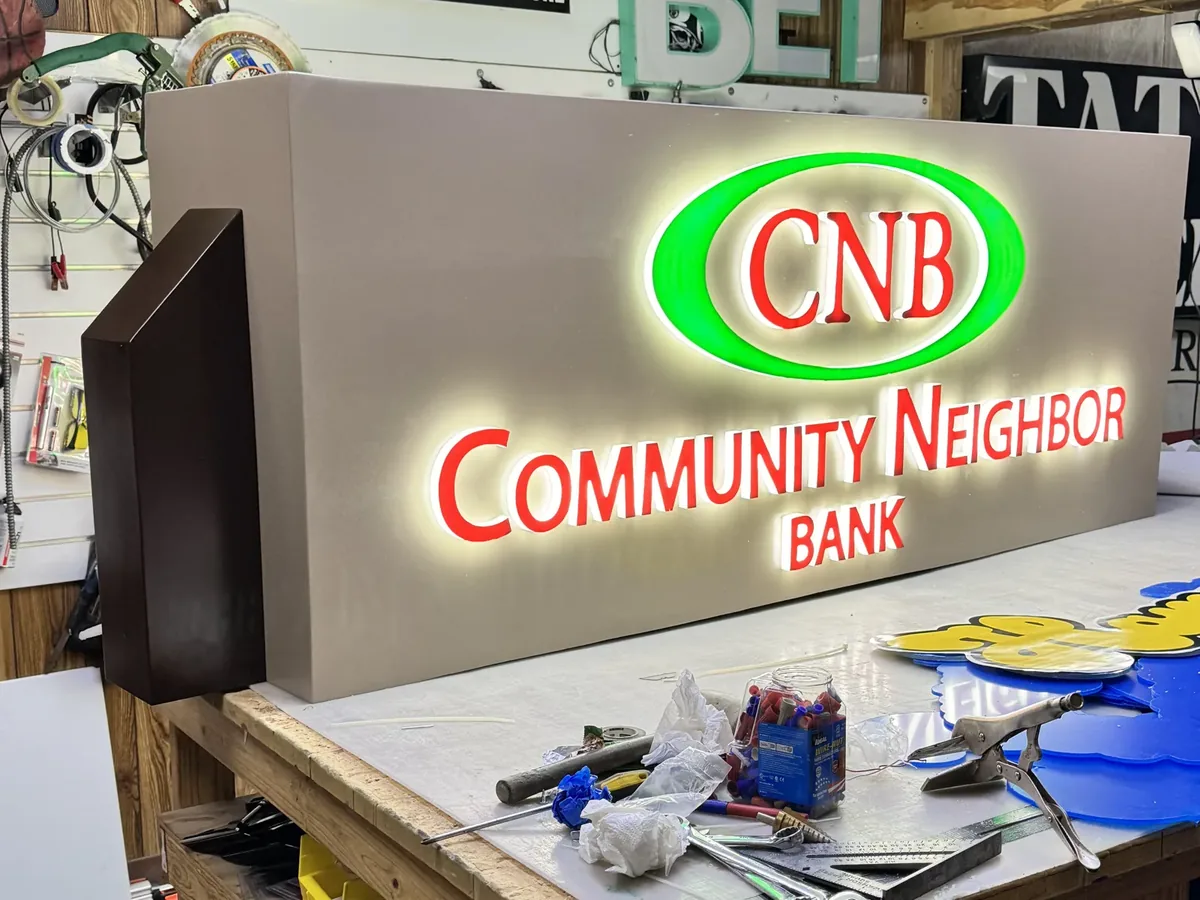 The Community Neighbor Bank monument sign face lit on a workbench in our sign shop: red letters inside a green ring, glowing on a grey face
