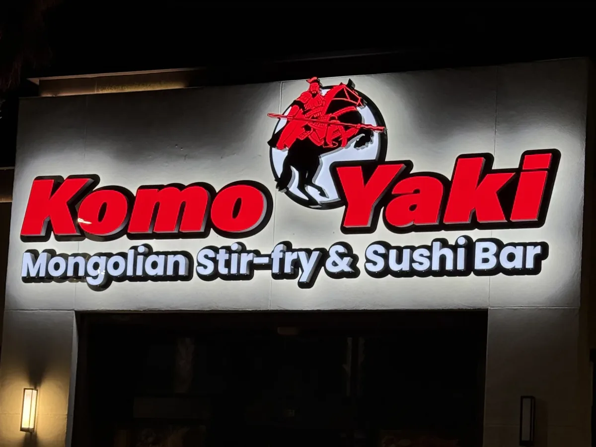 The Komo Yaki Mongolian Stir-fry & Sushi Bar channel letters lit at night, red above white with a red warrior logo, glowing on the restaurant front wall