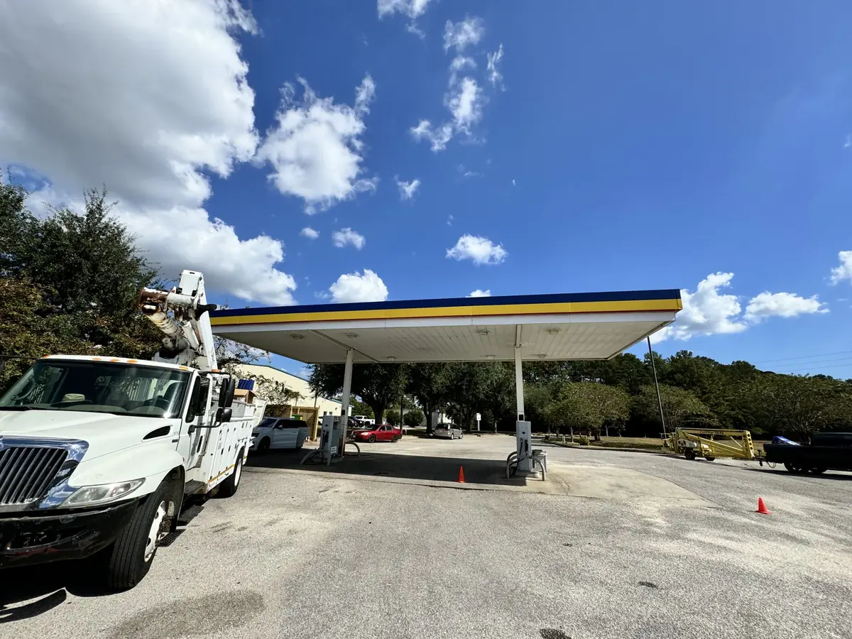 A bucket truck parked beside a fuel canopy, with a towable lift across the lot