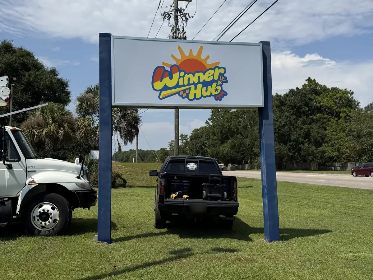 The Winner Hub two-post pylon sign by the road, with a bucket truck and a Sparks Sign Company pickup parked on the grass beside it