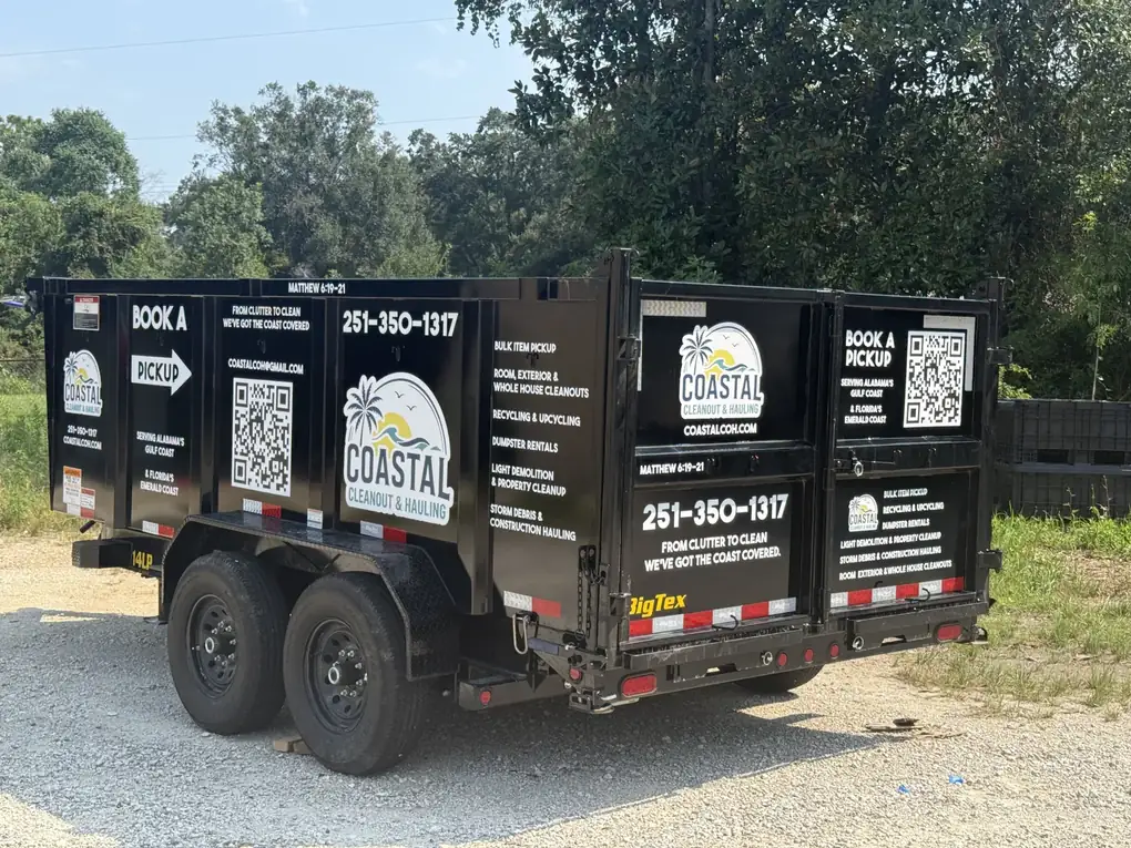 A Coastal Cleanout & Hauling dump trailer lettered on its black sides with the company logo, services and QR codes