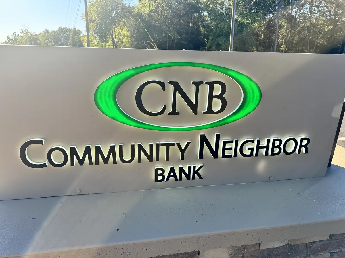 Community Neighbor Bank monument sign, its letters halo-lit and a green lit ring around CNB on the grey face, above a stone base