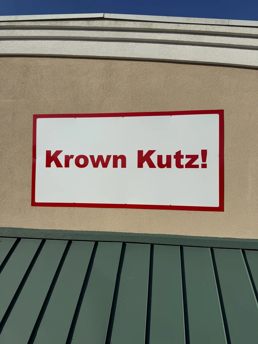 Krown Kutz! flat panel sign above a green metal awning