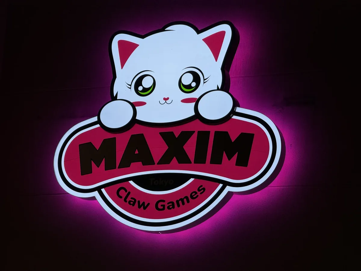 Maxim Claw Games cat logo sign lit at night with a pink halo glow on the wall