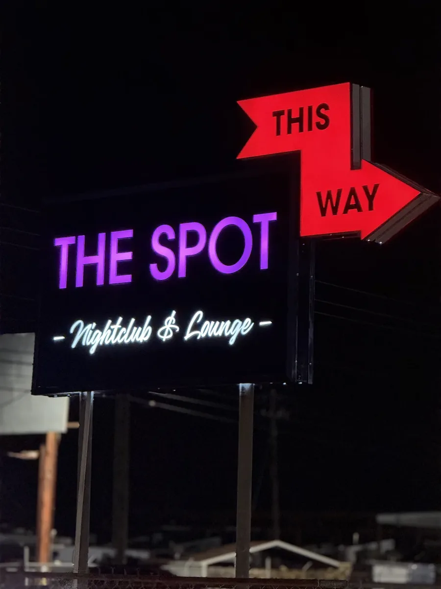 The Spot Nightclub & Lounge post sign lit purple at night with a red This Way arrow