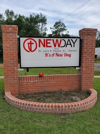 A church sign panel set between red brick pillars, with curved brick planter walls around its base