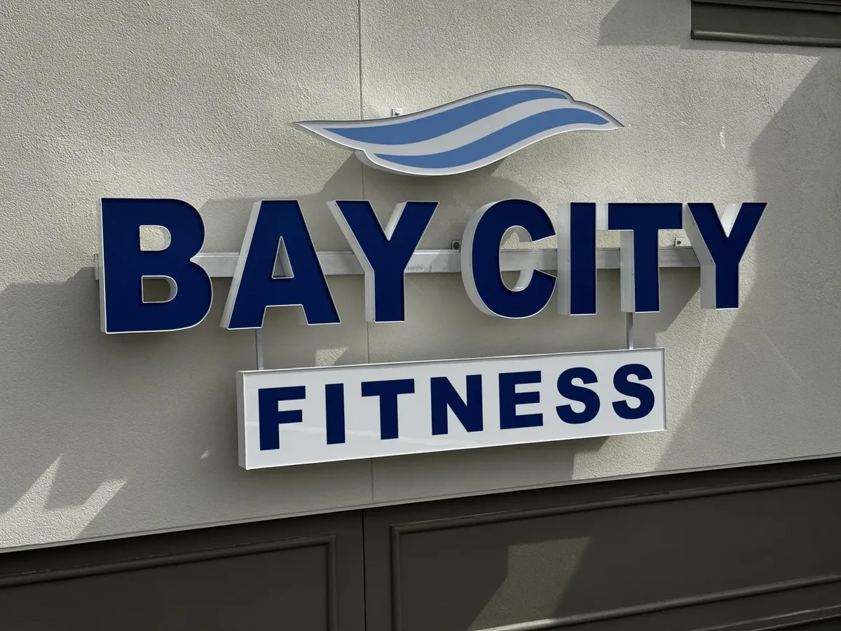 Navy Bay City Fitness channel letters with a blue wave logo and a Fitness panel on a stucco wall
