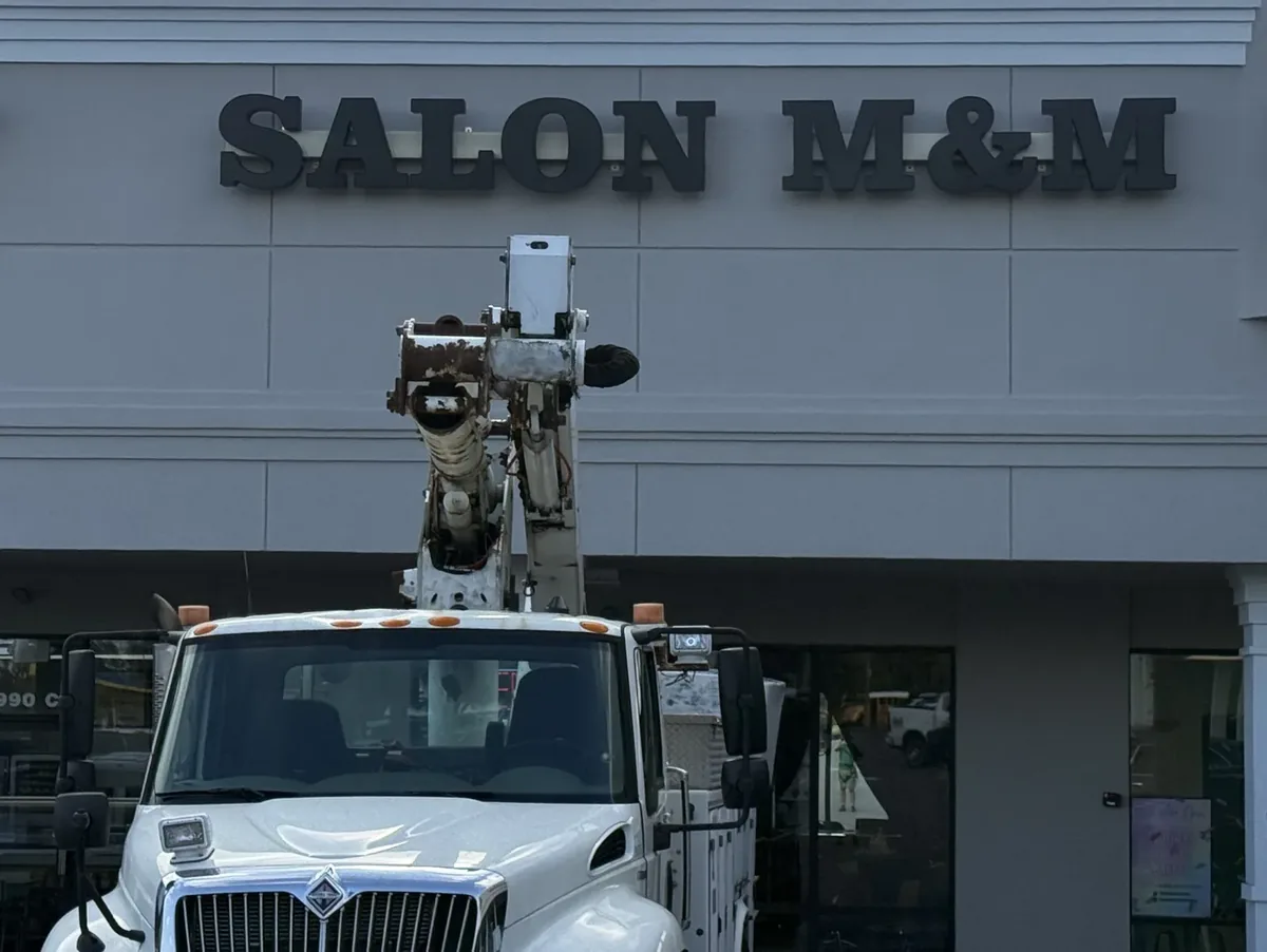 A white bucket truck parked below the new Salon M&M dimensional letters on a shopping-center facade