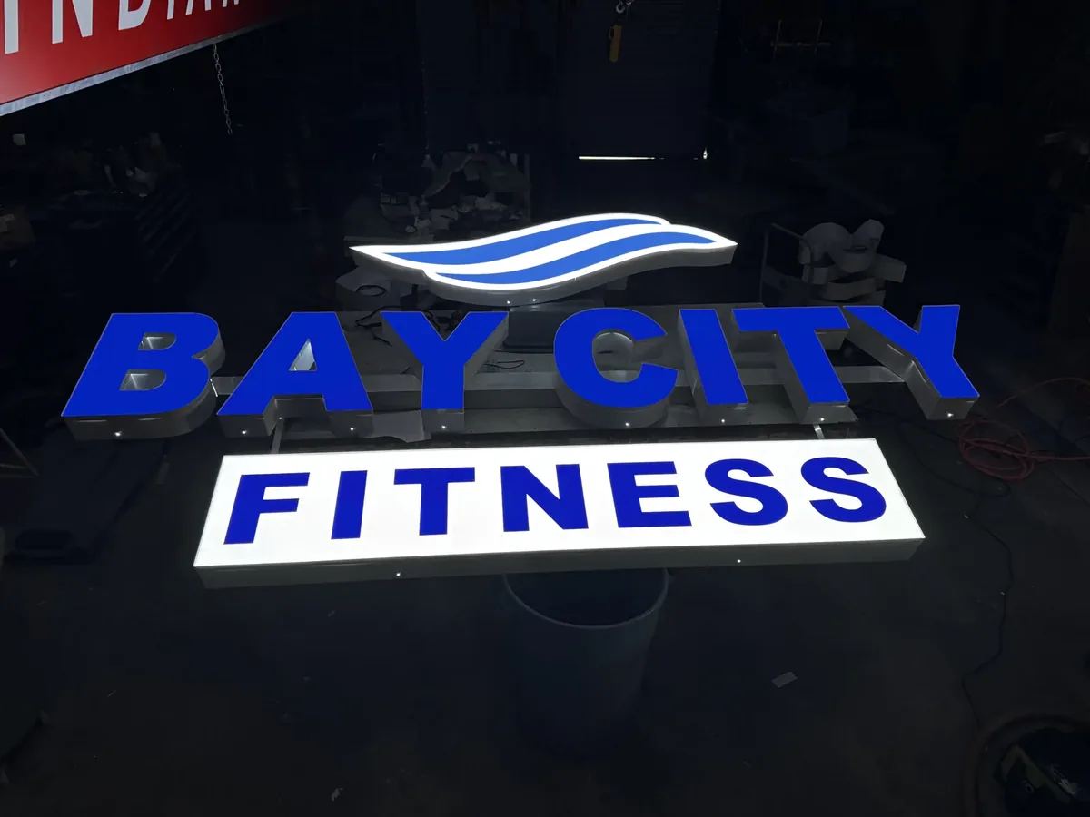 Bay City Fitness letters and panel lit during a light test in the darkened sign shop