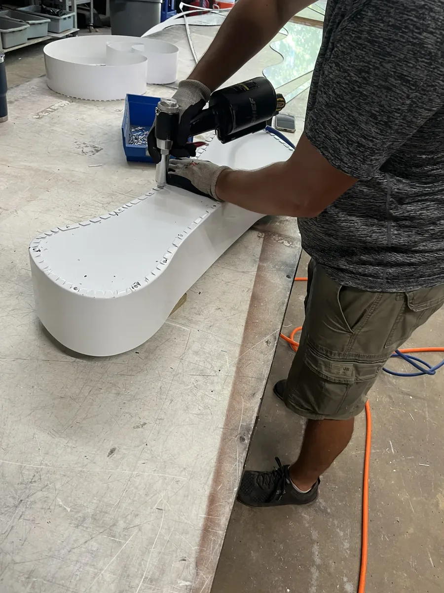 A Sparks crew member fastening the return of a white channel letter at a bench in the sign shop