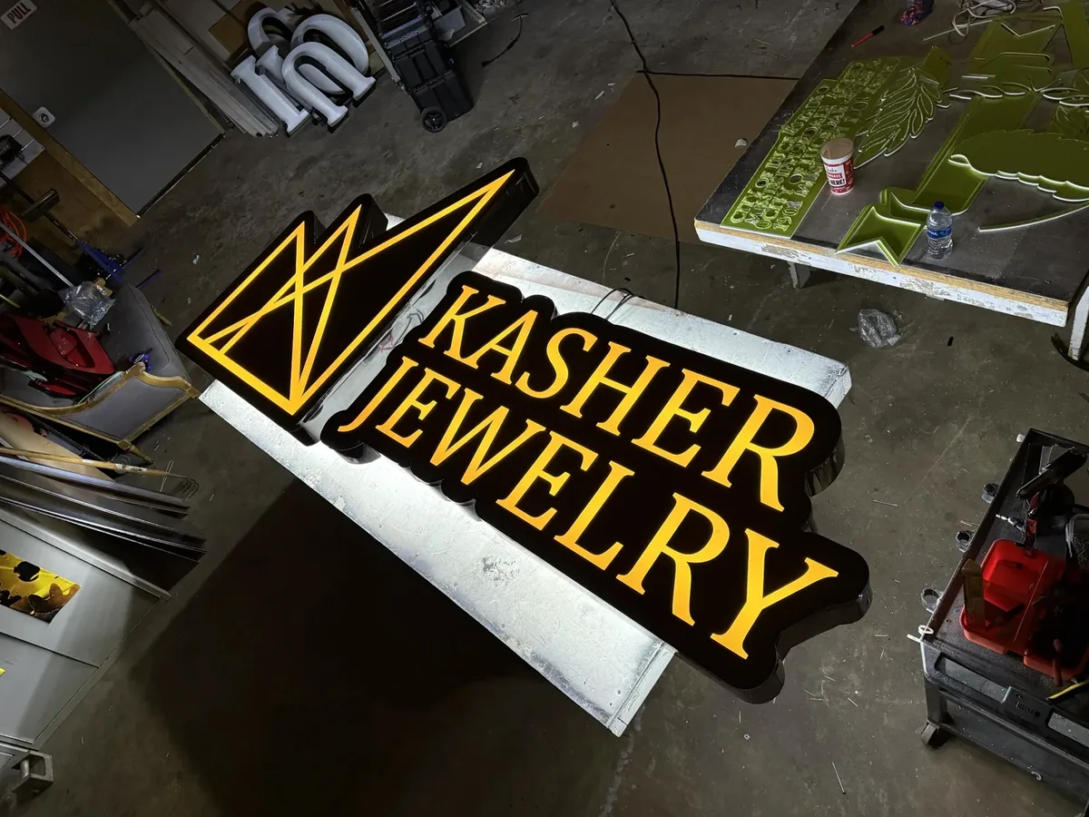 Gold-lit channel letters and a logo for a jewelry store on a bench in the sign shop