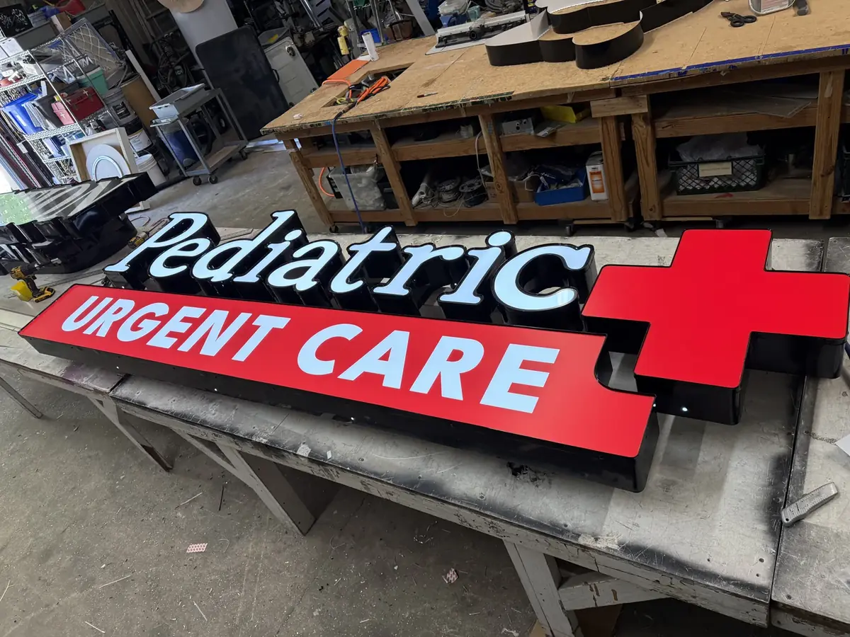 Pediatric Urgent Care channel letters and their red cross lit on a table in the sign shop