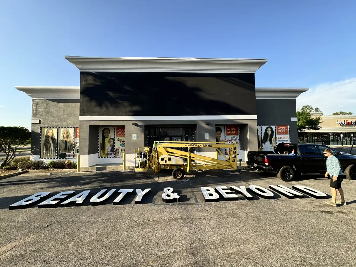 Beauty & Beyond letters laid out in order on the parking lot before mounting, with a towable lift parked at the storefront