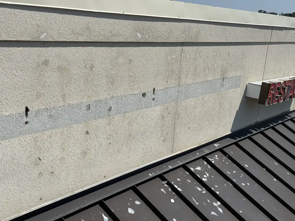 The same storefront fascia after sign removal, with only screw holes and a pale stripe left where the letters were