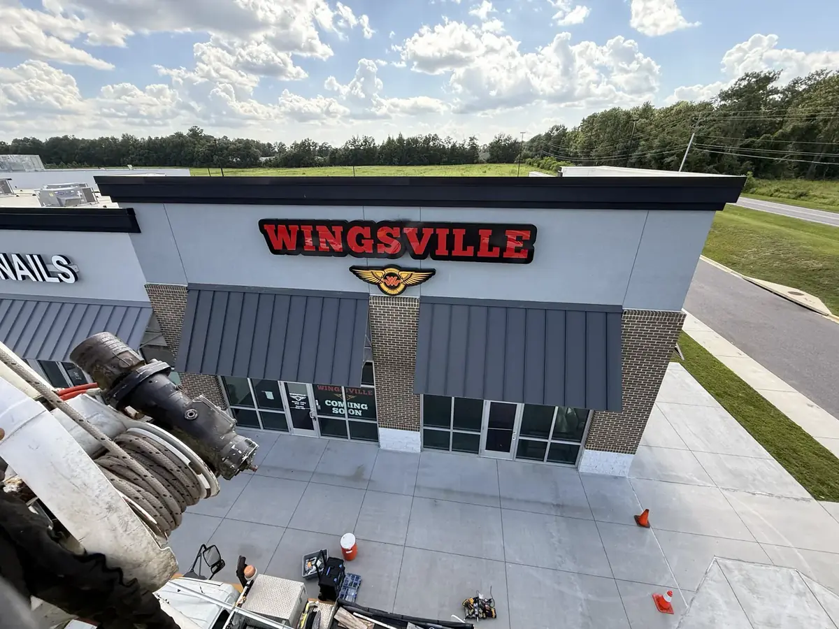 View from a bucket truck bucket looking down on the new Wingsville letters over the storefront, with cones and tools on the walk below