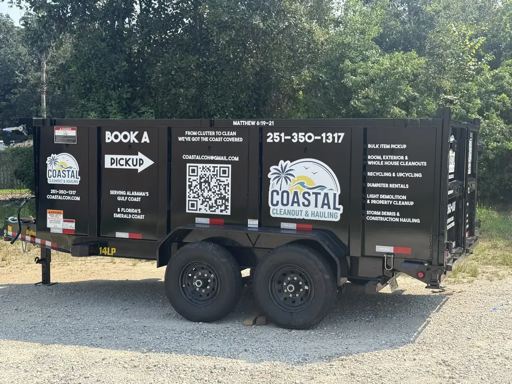 A black dump trailer lettered with a hauling company's logo, services, QR code and phone number