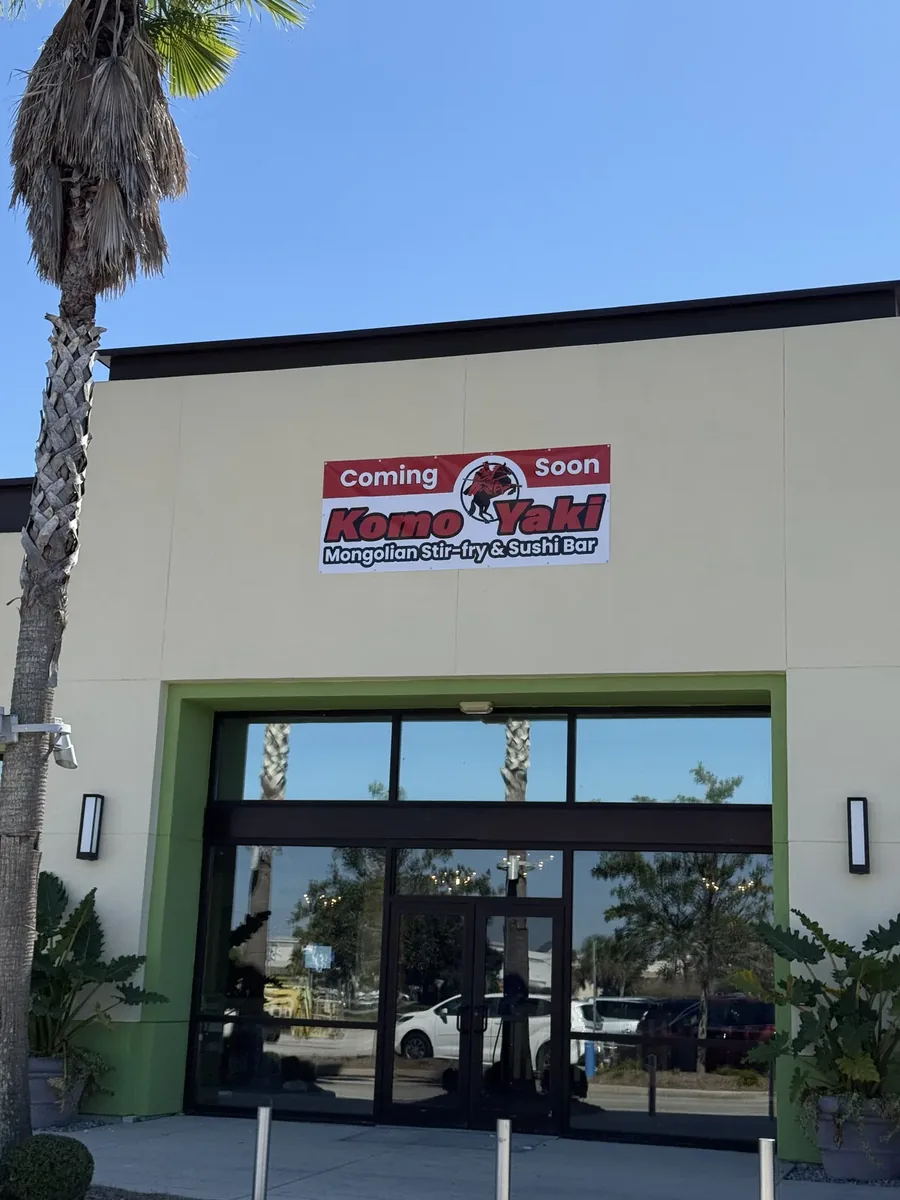 A red and white Coming Soon vinyl banner with a restaurant's logo hung on a cream facade above its glass entrance