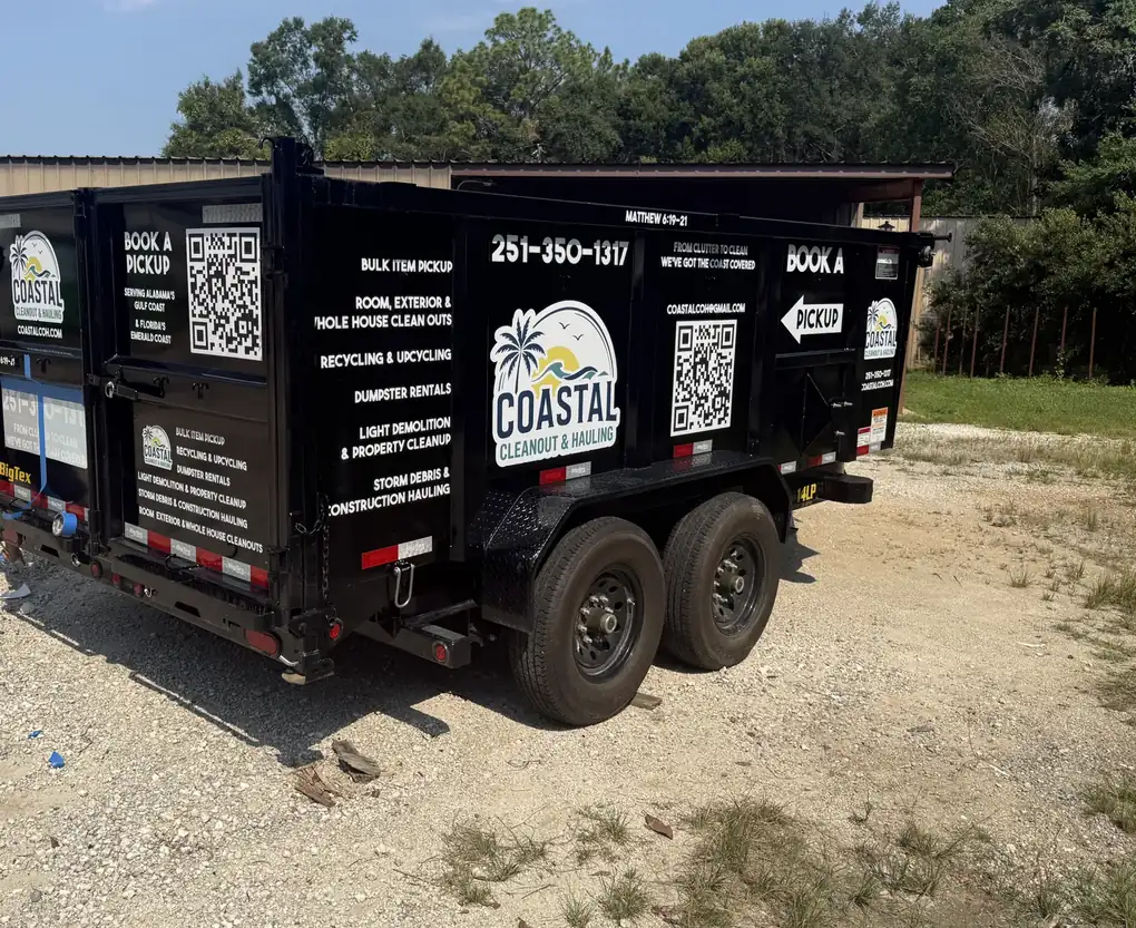 A black dump trailer lettered for Coastal Cleanout & Hauling: its logo, list of services, phone number and QR codes on the side and rear doors