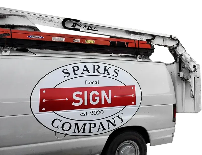 The Sparks Sign Company oval logo on the side door of a white bucket van with a ladder rack and lift boom