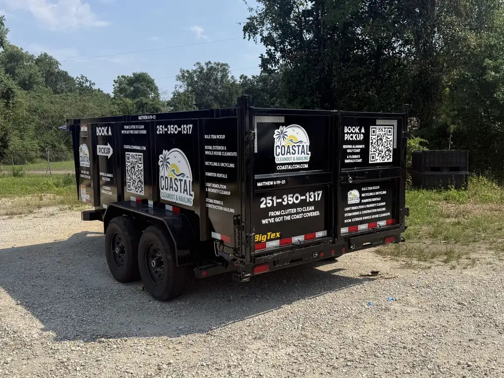 The rear and side of a black dump trailer lettered for Coastal Cleanout & Hauling, with its logo, services, phone number and QR codes on the panels and rear doors
