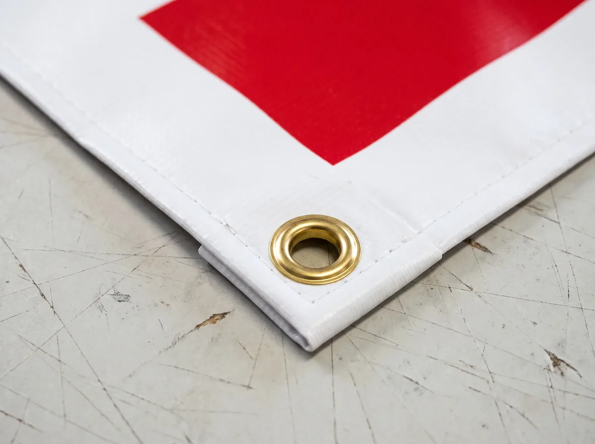 Close-up of a vinyl banner corner folded into a reinforced hem with a brass metal grommet