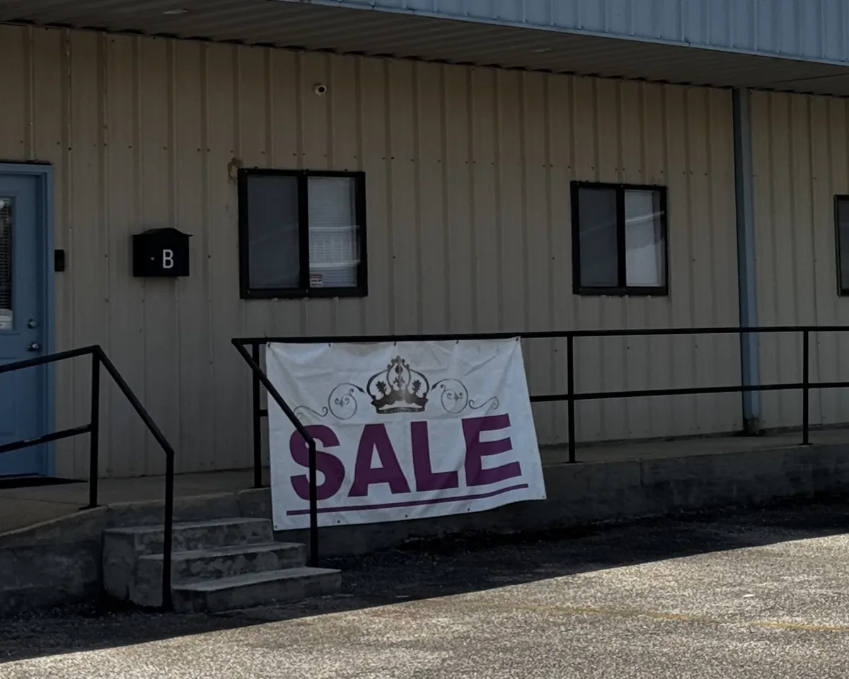 White SALE banner with a purple crown logo fastened by its grommets to the railing in front of the Righteous shoe and apparel store