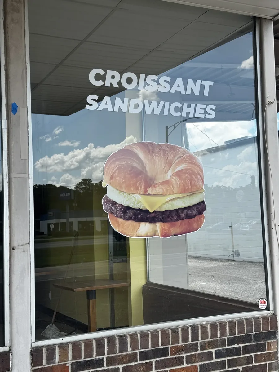 Lickin Good Donuts window with croissant sandwiches lettering above a cut-out croissant sandwich graphic