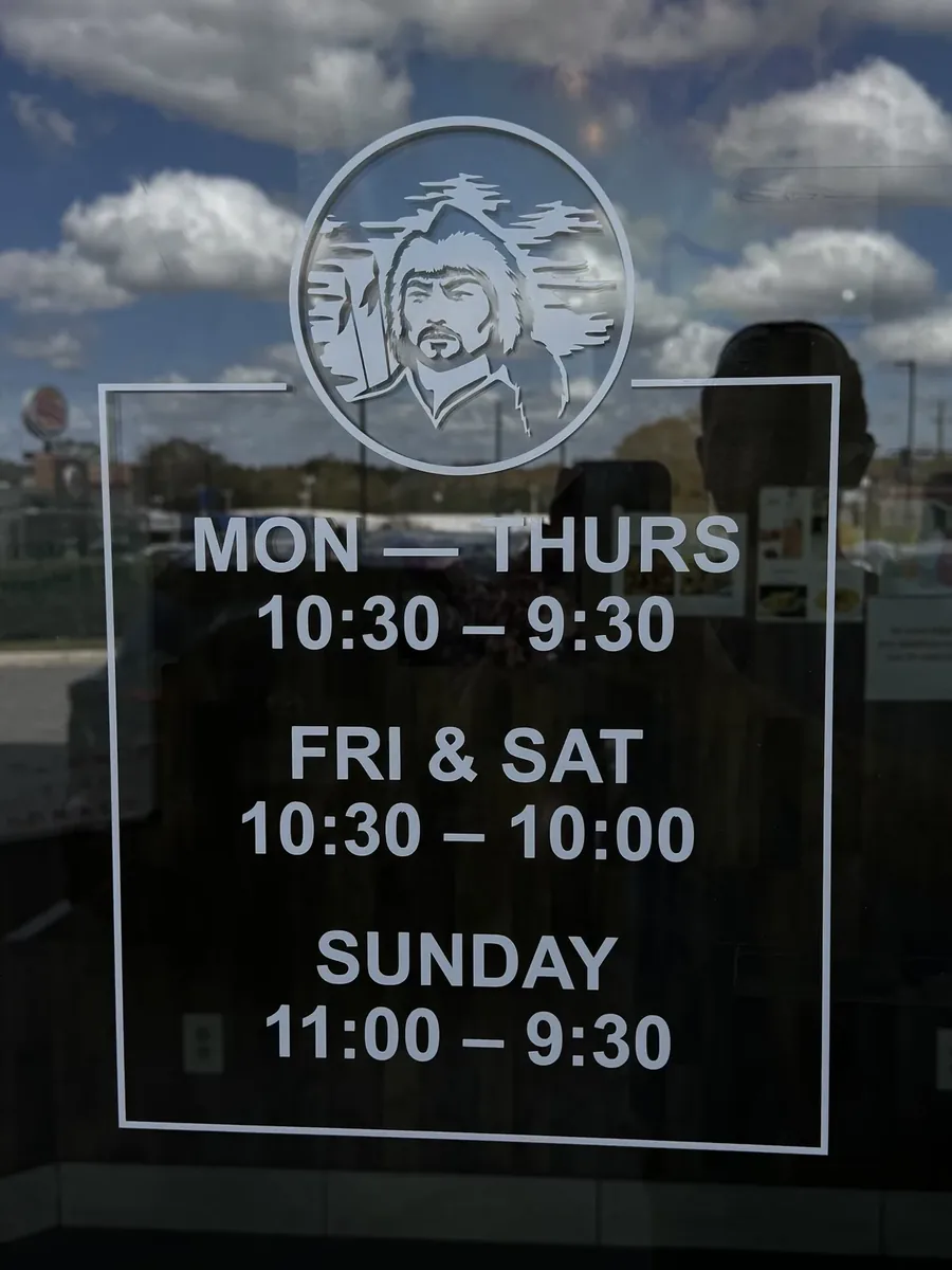A shop's opening hours and portrait logo in white vinyl lettering on a glass door